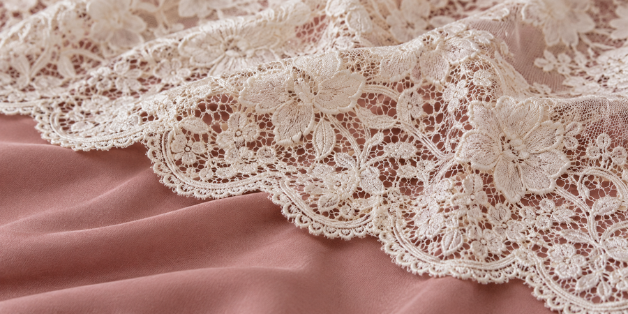 Detail van ivoorkleurig bloemkant op roze stof